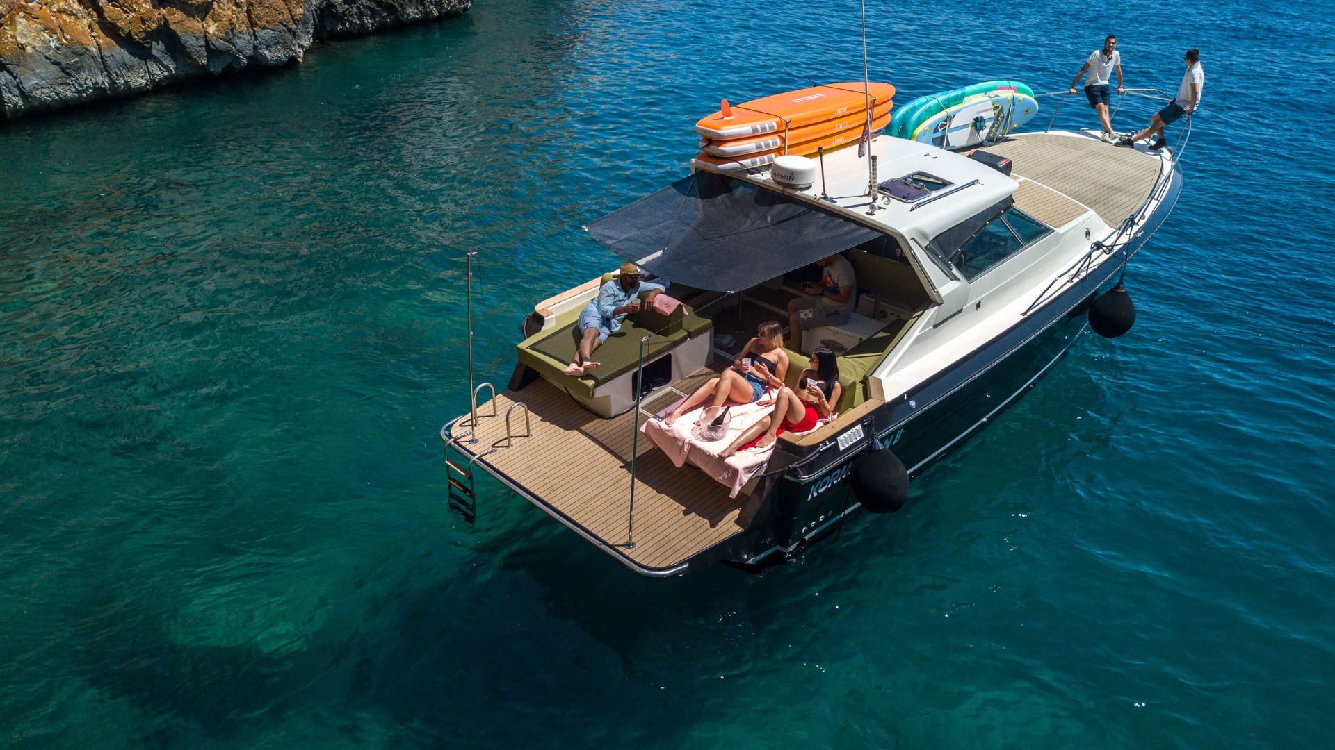 Aerial view of a luxury boat anchored in a secluded bay near Hvar, with guests relaxing on board and enjoying premium service surrounded by crystal-clear water.
