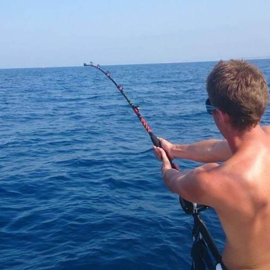 Man struggling to hold a fishing rod bent under the weight of a big catch during an intense fishing moment at sea near Hvar.