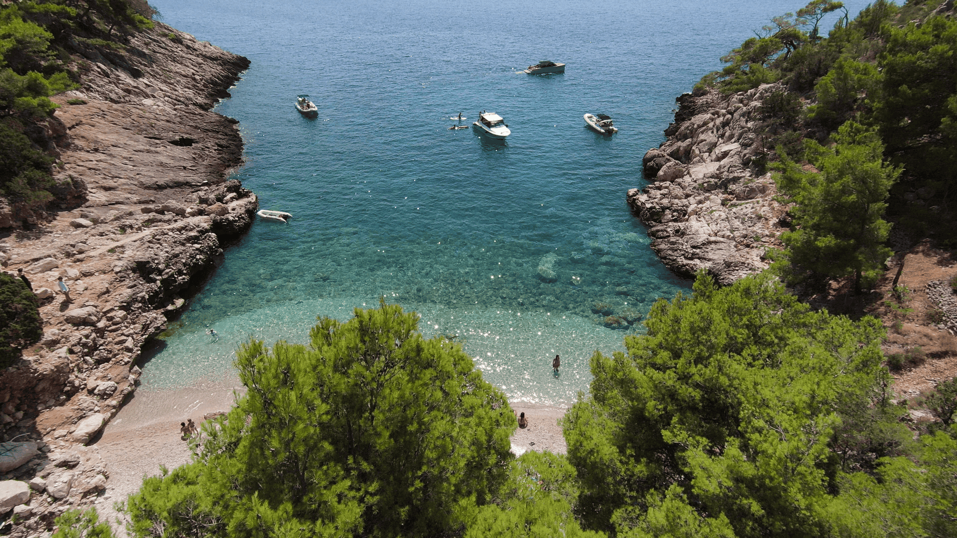 Blog what to bring on a boat tour in Hvar - view of a picturesque bay with a beach, surrounded by rocky cliffs and clear turquoise sea.